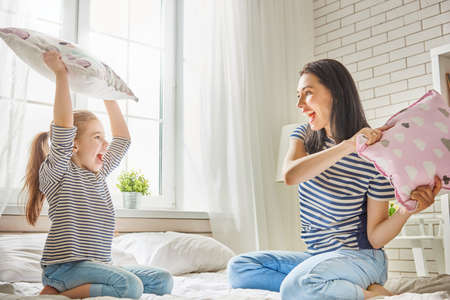 Happy loving family! The mother and her child girl are fighting pillows.の写真素材