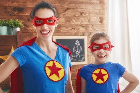 Mother and her child playing together. Girl and mom in Superhero costume. Mum and kid having fun,...