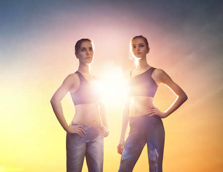 Healthy lifestyle and sport concepts. Women in fashionable sportswear do exercise on nature. Two beautiful girls on sunset background.の写真素材