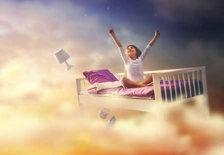 Kids dreams. Cute child girl is flying in her bed trough star sky.