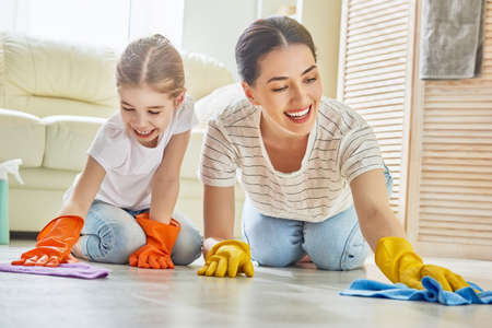 Happy family cleans the room. Mother and daughter do the cleaning in the house. A young woman and child girl are dusting. Cute little helper.の写真素材