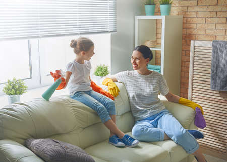 Happy family cleans the room. Mother and daughter do the cleaning in the house. A young woman and child girl are dusting. Cute little helper.の写真素材