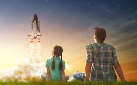 Dad and daughter watching how to fly a spaceship. Happy family on sunset background on nature.
