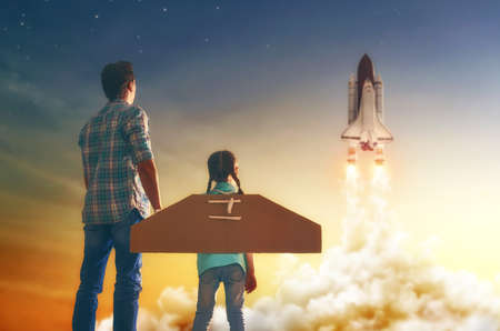 Dad and daughter watching how to fly a spaceship. Happy family on sunset background on nature.