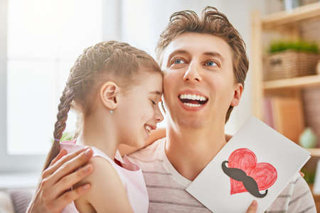 Happy father's day! Child daughter congratulates dad and gives him postcard. Daddy and girl smiling and hugging. Family holiday and togetherness.の写真素材
