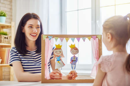 Happy loving family. Mother and her daughter in kids room. Funny mom and lovely child having fun and playing performance in the puppet theater indoors. Prince and princess.の写真素材