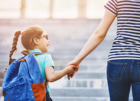 Parent and pupil of primary school go hand in hand. Woman and girl with backpack behind the back....