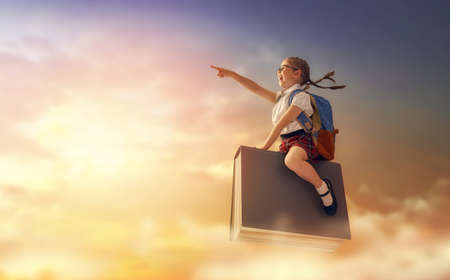 Back to school! Happy cute industrious child flying on the book on background of sunset sky. Concept of education and reading. The development of the imagination.の写真素材
