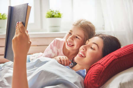 Pretty young mother reading a book to her daughter. Family holiday and togetherness.の写真素材