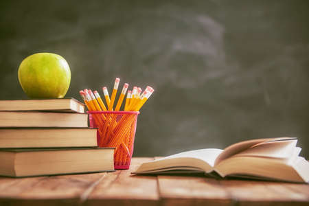Back to school and happy time! Apple and pile of books on the desk on background of blackboard.