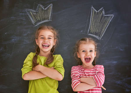 Funny children on a background of black board. Girls are having fun and drawing crowns. Concept of successful education.の写真素材