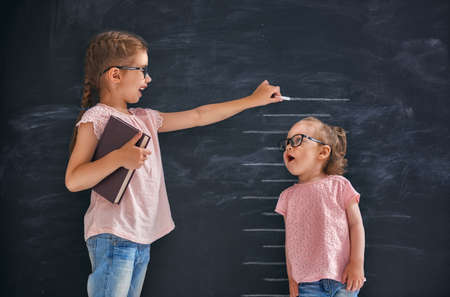 Two children sisters play together. Kid measures the growth on the background of blackboard. Concept of education.の写真素材