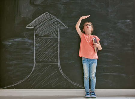 Cute child is playing. Kid measures the growth on the background of blackboard. Concept of education.の写真素材
