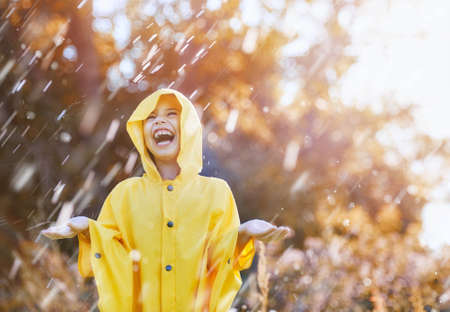 Happy funny child under the autumn shower. Girl is wearing yellow raincoat and enjoying rainfall.