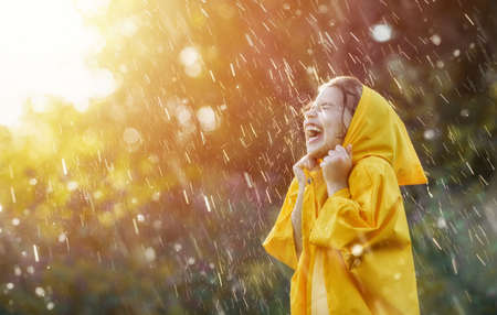 Happy funny child under the autumn shower. Girl is wearing yellow raincoat and enjoying rainfall.の写真素材