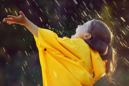 Happy funny child under the autumn shower. Girl is wearing yellow raincoat and enjoying rainfall. の写真素材