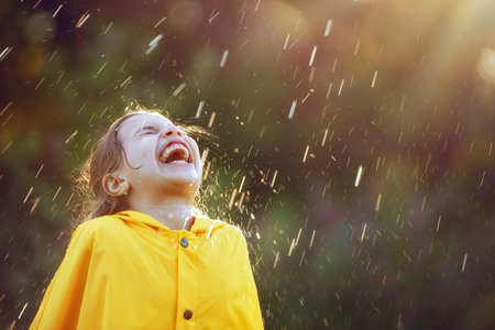Happy funny child under the autumn shower. Girl is wearing yellow raincoat and enjoying rainfall. の写真素材