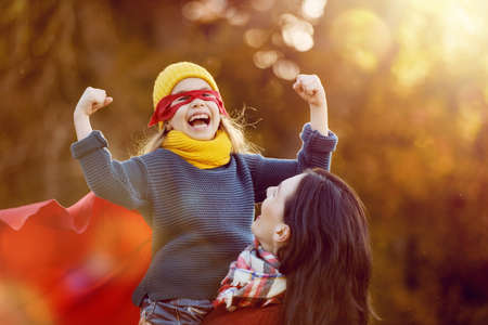 Happy family on autumn walk! Mother and daughter walking in the Park and enjoying the beautiful autumn nature. Child girl plays superhero.の写真素材