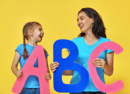Happy smiling child and teacher are having big letters. Yellow, blue and pink colors.の写真素材