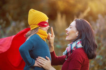 Happy family on autumn walk! Mother and daughter walking in the Park and enjoying the beautiful autumn nature. Child girl plays superhero.の写真素材