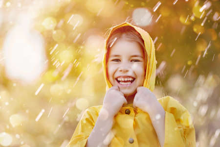 Happy funny child under the autumn shower. Girl is wearing yellow raincoat and enjoying rainfall. の写真素材
