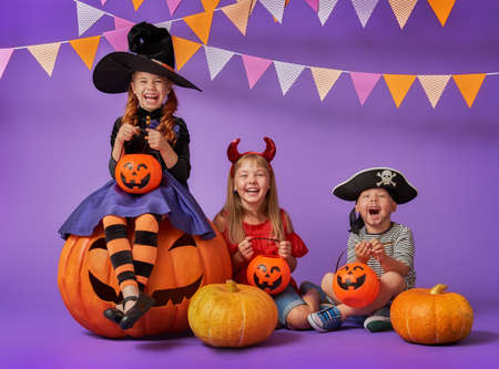 Happy brother and two sisters at Halloween. Funny kids in carnival costumes on background of purple wall. Cheerful children and pumpkins.の写真素材