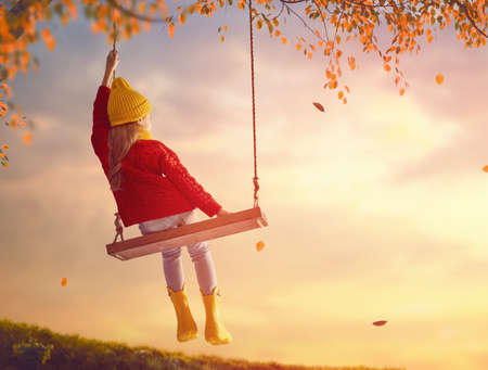 Happy child girl on swing in sunset fall. Little kid playing in the autumn on the nature walk.