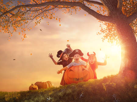 Happy brother and two sisters at Halloween. Funny kids in carnival costumes outdoors. Cheerful children and pumpkins on sunset background.の写真素材