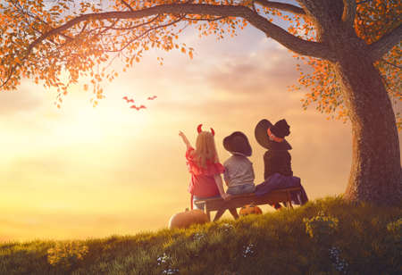 Happy brother and two sisters at Halloween. Funny kids in carnival costumes outdoors. Cheerful children and pumpkins on sunset background.の写真素材