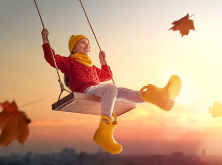 Happy child girl on swing in sunset fall. Little kid playing in the autumn on the nature walk.の写真素材