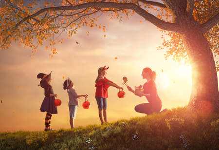 Happy family celebrating Halloween! Young mom treats children with candy. Funny kids in carnival costumes.の写真素材