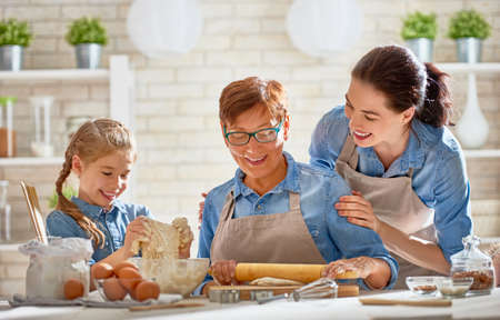 Happy loving family are preparing bakery together. Granny, mom and child daughter girl are cooking cookies and having fun in the kitchen. Homemade food and little helper.の写真素材