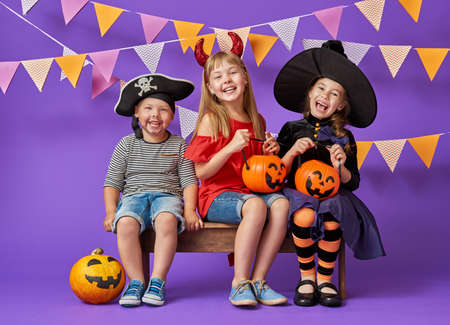 Happy brother and two sisters at Halloween. Funny kids in carnival costumes on background of purple wall. Cheerful children and pumpkins.の写真素材