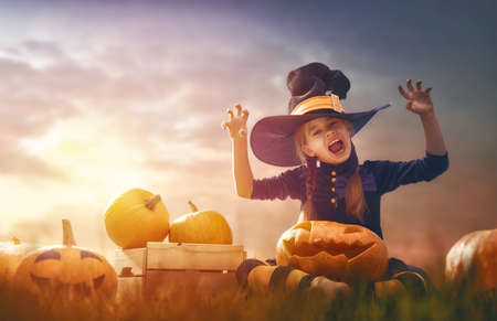 Happy Halloween! Cute little witch with pumpkins. Beautiful young child girl in costume outdoors.の写真素材