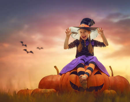 Happy Halloween! Cute little witch with pumpkins. Beautiful young child girl in costume outdoors.の写真素材