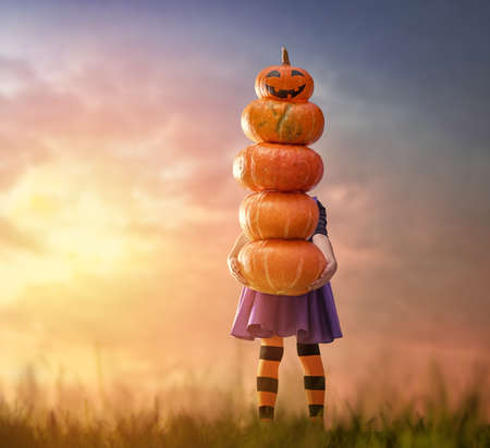 Happy Halloween! Cute little witch with pumpkins. Beautiful young child girl in costume outdoors.の写真素材