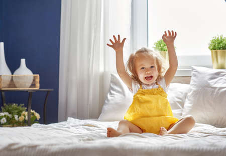Beautiful smiling cute baby girl on the bed in the room at home. Happy child laughing.の写真素材