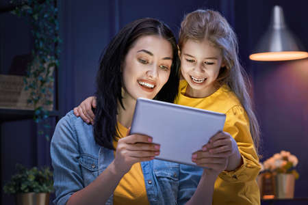 Happy loving family. Young mother and her daughter girl are playing in bedroom. Funny mom and lovely child are having fun with tablet.の写真素材