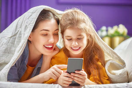 Happy loving family. Young mother and her daughter girl are playing in bedroom. Funny mom and lovely...