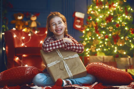 Merry Christmas and Happy Holidays! Cheerful cute little child girl. Kid near tree indoors.の写真素材