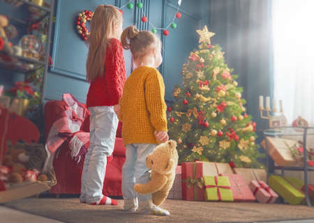 Merry Christmas and Happy Holidays! Cheerful cute little children girls. Kids sisters near tree indoors.の写真素材