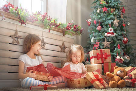 Merry Christmas and Happy Holidays! Cheerful cute childrens girls opening gifts. Kids wearing pajamas having fun near tree in the morning. Loving family with presents in room.の写真素材