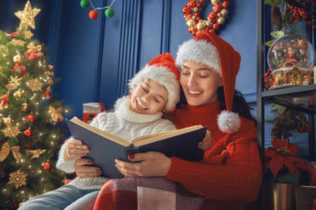 Merry Christmas! Pretty young mother reading a book to her daughter near Christmas tree.の写真素材