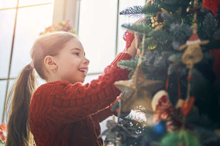 Merry Christmas and Happy Holidays! Cute little child girl is decorating the tree indoors. The morning before Xmas. Portrait kid close up.の写真素材