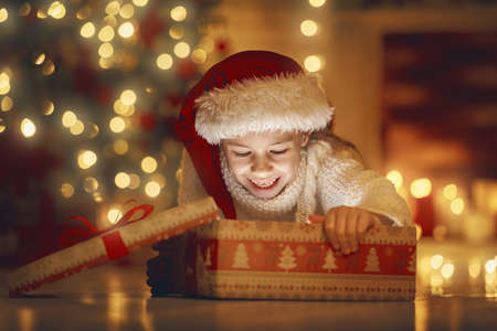 Merry Christmas and Happy Holiday! Cute little child girl with present gift box near tree at home.の写真素材