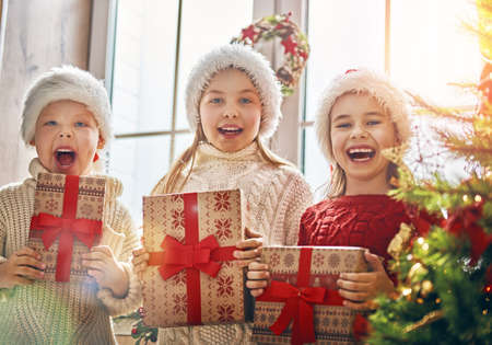 Merry Christmas and Happy Holidays! Cheerful cute children opening gifts. Kids having fun near tree in the morning. Loving family with presents in room.の写真素材