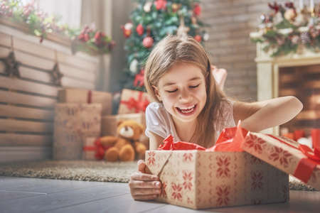Happy holidays! Cute little child opening present near Christmas tree. The girl laughing and enjoying the gift. の写真素材