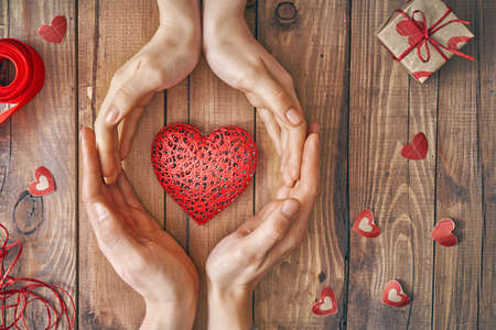 Hands of man and woman holding red heart on wooden background. Concept of Valentine's Day. Top view. Close up.の写真素材