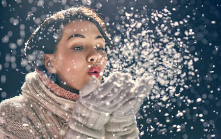 Happy young woman blowing on snow on winter walk in nature. Concept of frost winter season.の写真素材