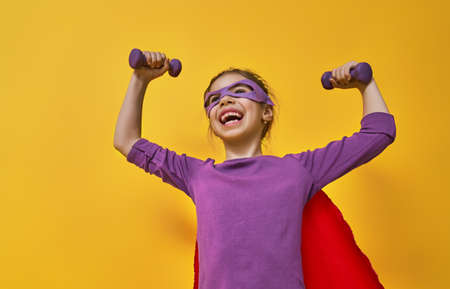 Little child is playing superhero. Kid on the background of bright ultra violet wall. Girl power concept. Yellow, red and  purple colors.の写真素材